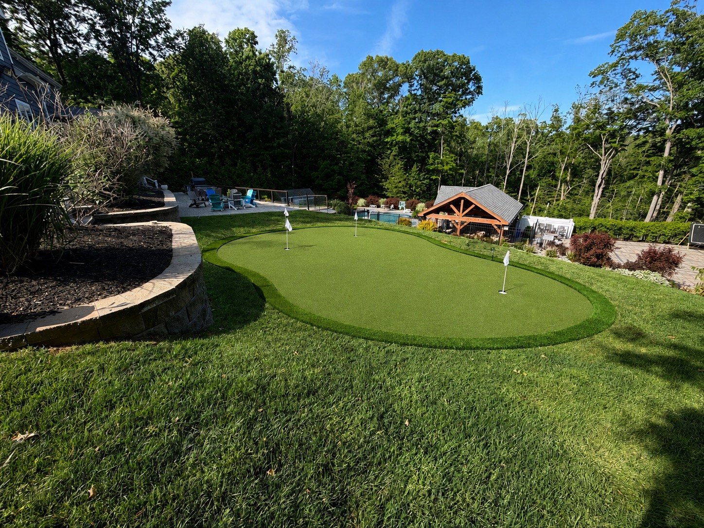 Completed backyard golf complex beside a pool and landscaped seating areas