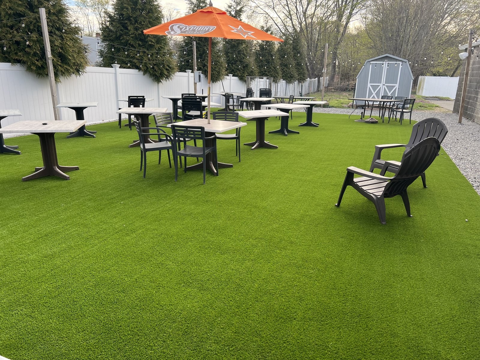 Outdoor dining tables, chairs and an orange umbrella on turf at Penny Lane Pub