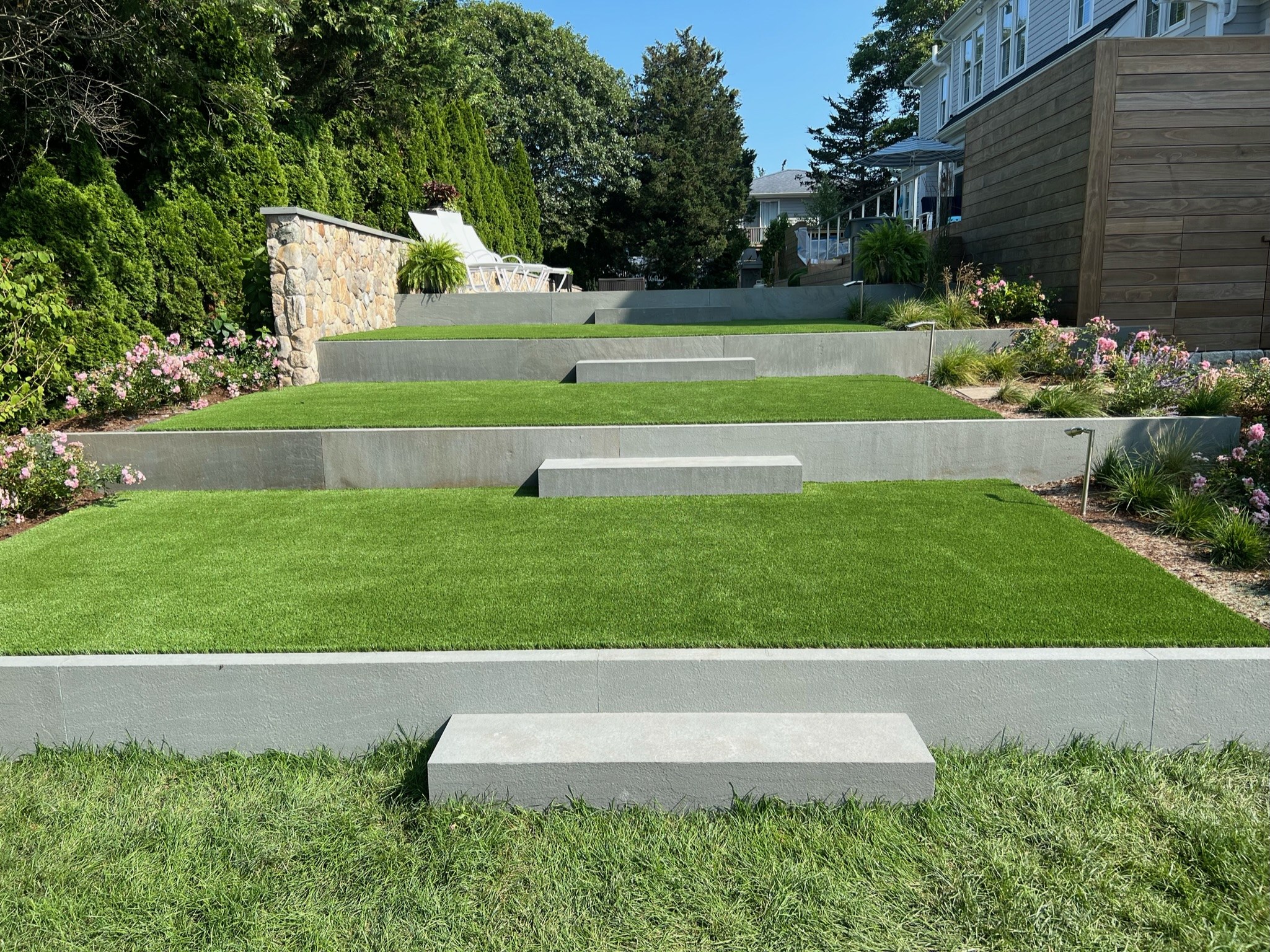 Synthetic lawn on three terraces with gray retaining walls, steps and planting