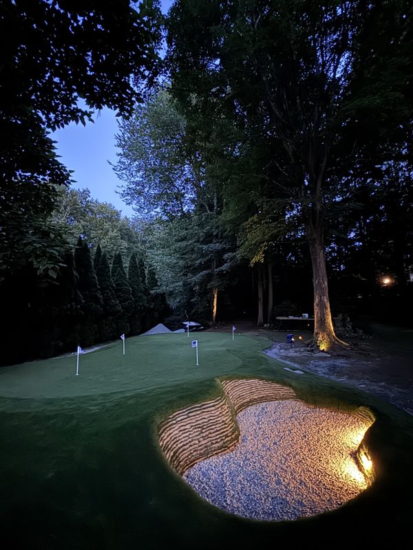 Golf Complex and illuminated sand bunker at dusk beneath mature trees.