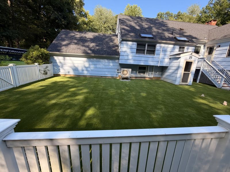 Residential turf lawn enclosed by white fencing beside a house and deck.