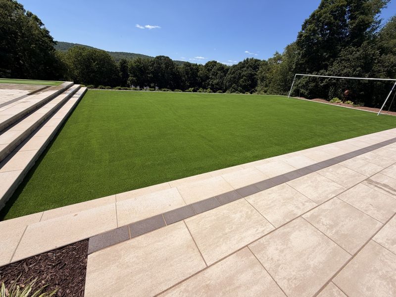 Broad turf recreation lawn beside a stone terrace with a net at the far edge