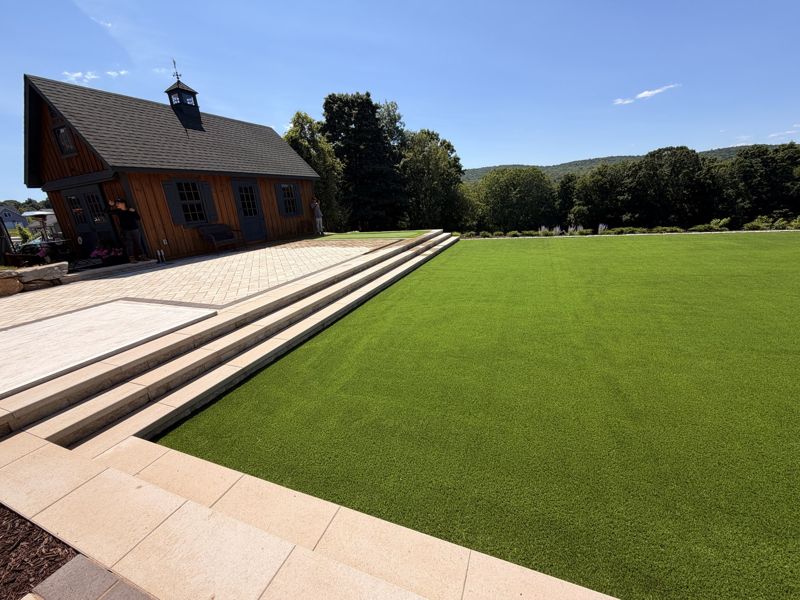 Wide view across a turf lawn from a stone terrace beside a timber building.