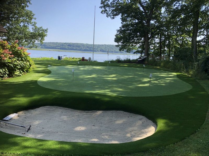 A golf complex and sand bunker framed by trees beside the water.