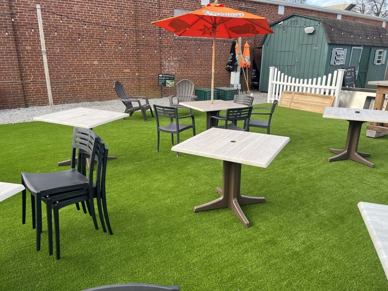 Tables, chairs and umbrellas arranged across a turf dining area.
