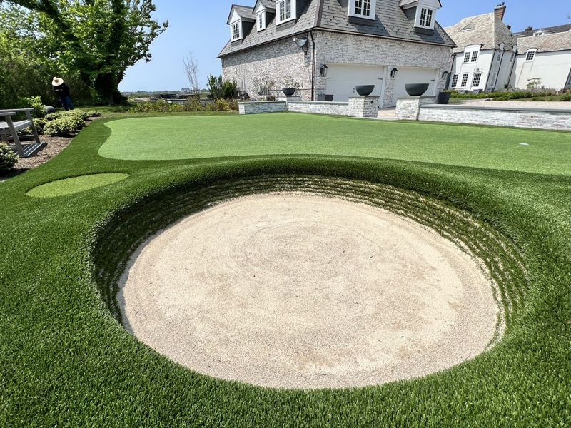 Finished golf complex with fringe and a circular sand bunker beside a stone coastal home