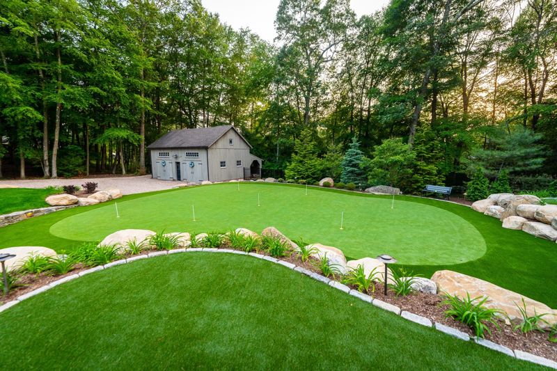 Finished curving backyard golf complex and fringe, with a stone planting border and small barn in Manchester, Connecticut