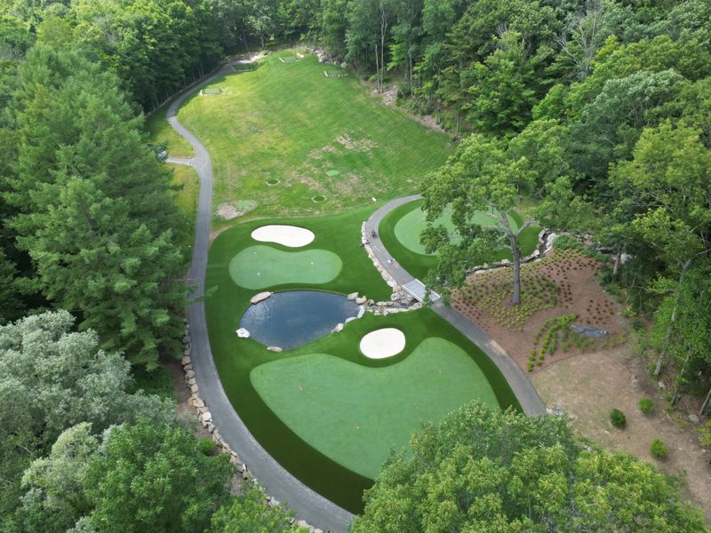 Aerial view of several synthetic golf greens and a white sand bunker in a wooded landscape